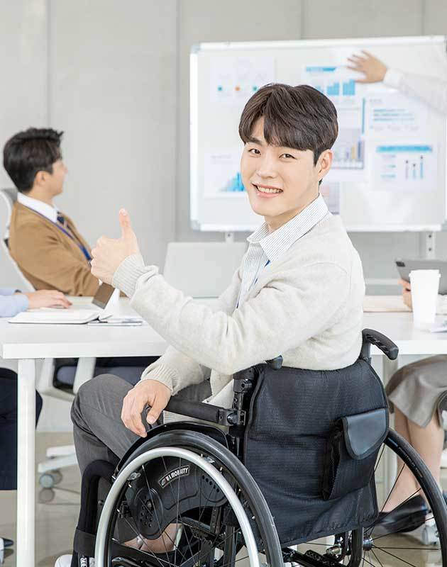 휠체어를 탄 남성이 엄지손가락을 펼치고 미소짓고 있는 이미지